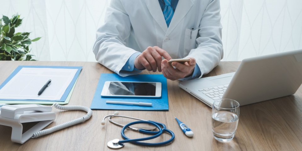 Professional doctor working at office desk, he is using a smartphone, healthcare and technology concept